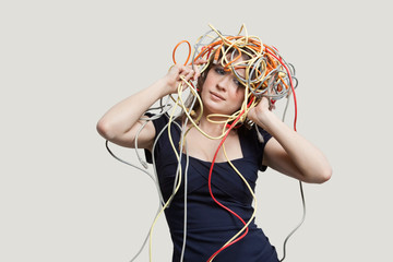 Young woman with head tangled in colorful cables over gray background