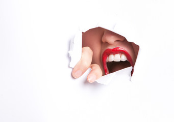 Close-up of furious young woman with red lips trying to break free from paper wall