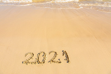 New Year 2021 is coming - inscription 2021 on a beach sand, the wave is starting to cover the digits - Summer beach holiday 2021 season golden sand - old year - message handwritten - empty copy space