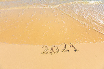 New Year 2021 is coming - inscription 2021 on a beach sand, the wave is starting to cover the digits - Summer beach holiday 2021 season golden sand - old year - message handwritten - empty copy space