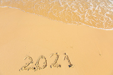 New Year 2021 is coming - inscription 2021 on a beach sand, the wave is starting to cover the digits - Summer beach holiday 2021 season golden sand - old year - message handwritten - empty copy space