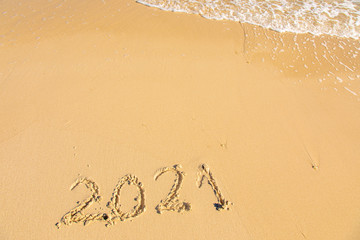 New Year 2021 is coming - inscription 2021 on a beach sand, the wave is starting to cover the digits - Summer beach holiday 2021 season golden sand - old year - message handwritten - empty copy space