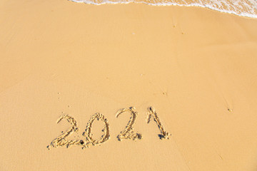 New Year 2021 is coming - inscription 2021 on a beach sand, the wave is starting to cover the digits - Summer beach holiday 2021 season golden sand - old year - message handwritten - empty copy space