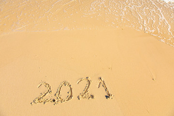 New Year 2021 is coming - inscription 2021 on a beach sand, the wave is starting to cover the digits - Summer beach holiday 2021 season golden sand - old year - message handwritten - empty copy space
