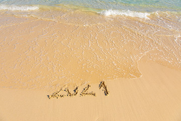New Year 2021 is coming - inscription 2021 on a beach sand, the wave is starting to cover the digits - Summer beach holiday 2021 season golden sand - old year - message handwritten - empty copy space