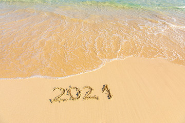 New Year 2021 is coming - inscription 2021 on a beach sand, the wave is starting to cover the digits - Summer beach holiday 2021 season golden sand - old year - message handwritten - empty copy space