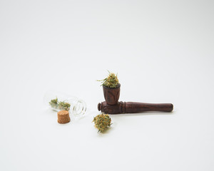 wooden marijuana smoking pipe next to a glass bottle with cannabis buds on a white background