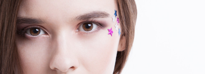 Fototapeta premium Cropped image of beautiful young woman with stars on her face against white background