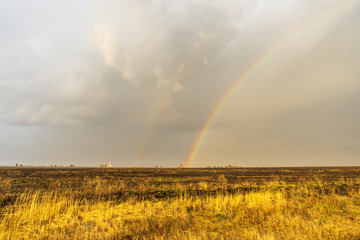 Spring landscape with double rainbow over burned field after thunderstorm. Beautiful natural background