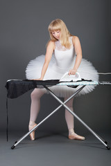 Young female ballet dancer ironing over grey background © MDBPIXS