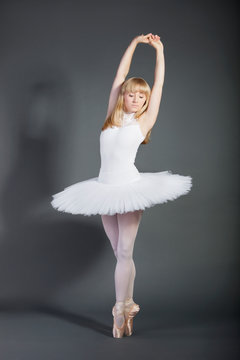 Young female ballet dancer tiptoeing over grey background