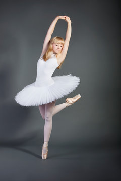Young woman in white tutu performing ballet over grey background