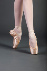 Low section of young female ballet dancer with legs crossed tiptoeing over grey background © MDBPIXS