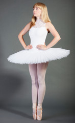 Young female ballet dancer in wearing tutu tiptoeing over grey background © MDBPIXS