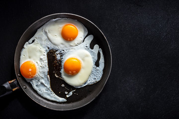 Fried eggs of three eggs in a pan. Black background
