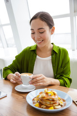 Smiling asian woman having pancakes for breakfast