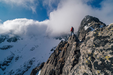 An alpinist standing on top of a high rock and watching winter mountain alpine landscape. Hiker or...