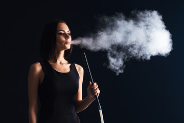 Young woman smoke a hookah on black wall background. The pleasure of smoking. Sexy smoke with vape....