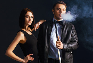 Love couple relaxing and smoking hookah on black wall background. The pleasure of smoking.  Exhaling smoke. Thick smoke from the hooka.