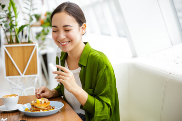 Smiling asian woman having pancakes for breakfast