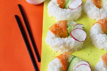 Sushi donuts with raw carrots, cucumber and radish on yellow orange paper background. Contemporary food concept, trendy Asian dinner for vegan or vegetarian, close up, top view