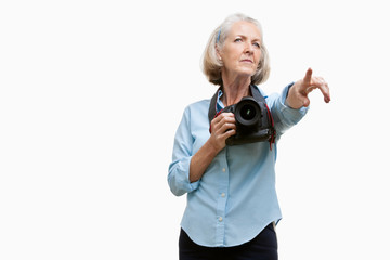 Senior female photographer with camera gesturing against white background