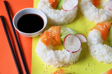 Sushi donuts with raw carrots, cucumber and radish on yellow orange paper background. Contemporary food concept, trendy Asian dinner for vegan or vegetarian, close up, top view