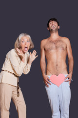 Shocked senior woman with young man holding red paper heart against black background