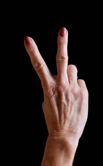 Senior woman's hands gesturing peace sign against black background