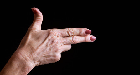 Senior woman's hands making shooting gesture against black background