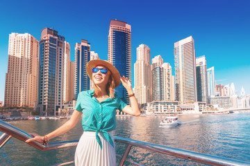 Fototapeta na wymiar Cheerful girl traveler on a ferry boat sailing through Dubai Marina port among huge skyscrapers. Concept of tourism in the UAE