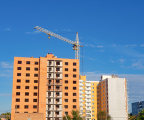 Fototapeta na wymiar Facade of unfinished brick condominium under construction with crane under blue sky