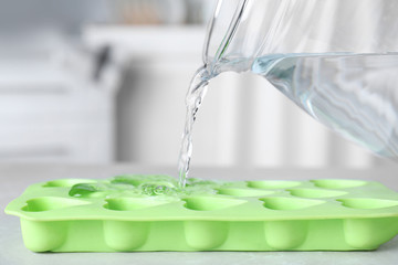 Pouring water into ice cube tray on table, closeup