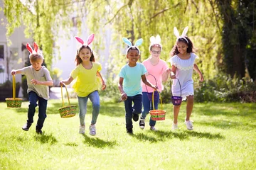 Foto op Plexiglas Group Of Children Wearing Bunny Ears Running To Pick Up Chocolate Egg On Easter Egg Hunt In Garden © Monkey Business