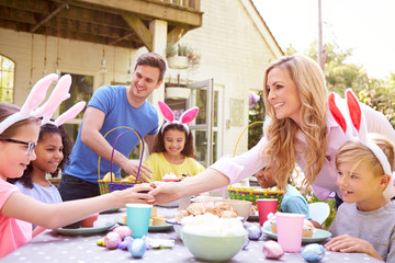 Parents With Children Wearing Bunny Ears Enjoying Outdoor Easter Party In Garden At Home