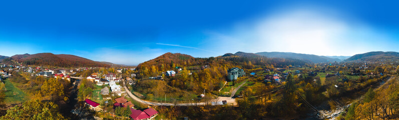 Aerial panoramic view of the village of Sheshory, surrounded by the Carpathian mountains. Buildings and infrastructure. The nature of Ukraine. Sunny autumn day. Huk waterfall on the Pistynka River. - obrazy, fototapety, plakaty