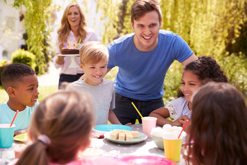 Parents And Son Celebrating Birthday With Friends Having Party In Garden At Home