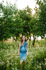 Pregnant happy girl go, with round stomach, go on grass in the outdoor in the garden background with trees. Close up. full length. Looking at camera