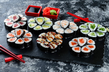 Set of sushi rolls with salmon on dark stone served with ginger and wasabi and wooden black wooden table. Fresh Japanese cuisine. Close up view on asian food. Sushi image for menu.