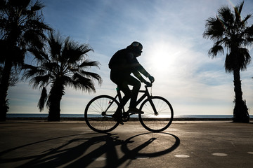 contraluz de hombre en bicicleta paseando por el paseo marítimo