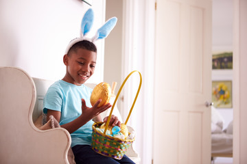 Boy Wearing Bunny Ears Sitting On Seat Holding Chocolate Egg He Has Found On Easter Egg Hunt