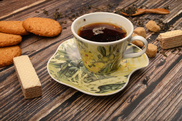 A Cup of black tea, tea leaves, pieces of brown sugar, oatmeal cookies, waffles on a wooden background. Close up.