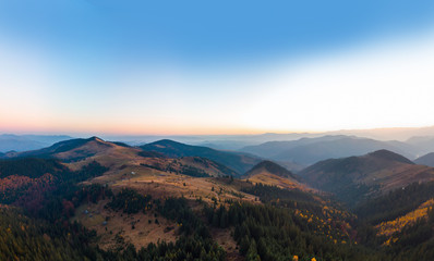 Naklejka na ściany i meble Aerial view of the Carpathian mountains in autumn. Pine forest, houses on the peaks, yellow fields and trees. Mountain meadow. sunset, Ukraine, Europe