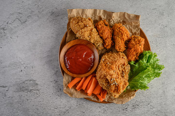 Crispy fried chicken on a wooden plate with tomato sauce and carrot. © Johnstocker