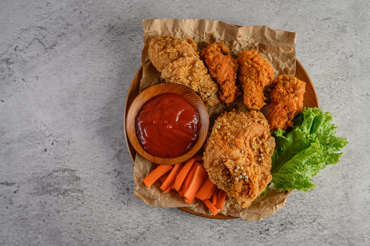 Crispy fried chicken on a wooden plate with tomato sauce and carrot.