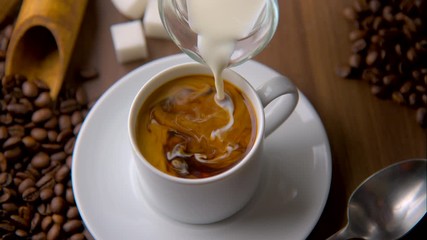 pouring milk in hot black coffee