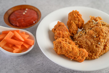 Crispy fried chicken on a white plate with tomato sauce and carrot,