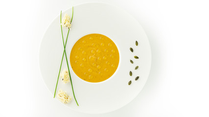 Sweet potato and carrot soup with some olive oils drops in a white plate with some pumpkin seeds, green onion feathers and three small peaces of bread