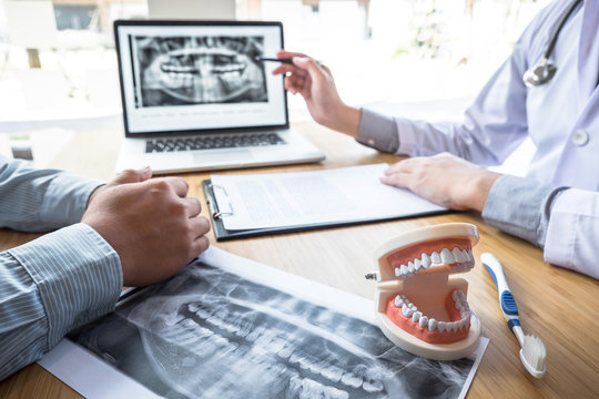Professional Dentist showing  jaw and teeth the x-ray photograph and discussing during explaining the consultation treatment issues with patient and writing history list on report