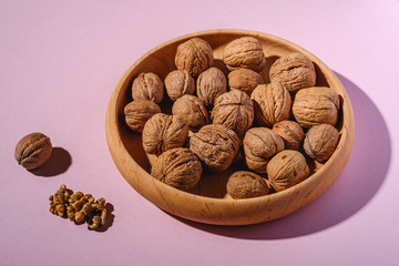 Walnuts heap food in wooden bowl on pink background near to peeled nuts, angle view, healthy food concept